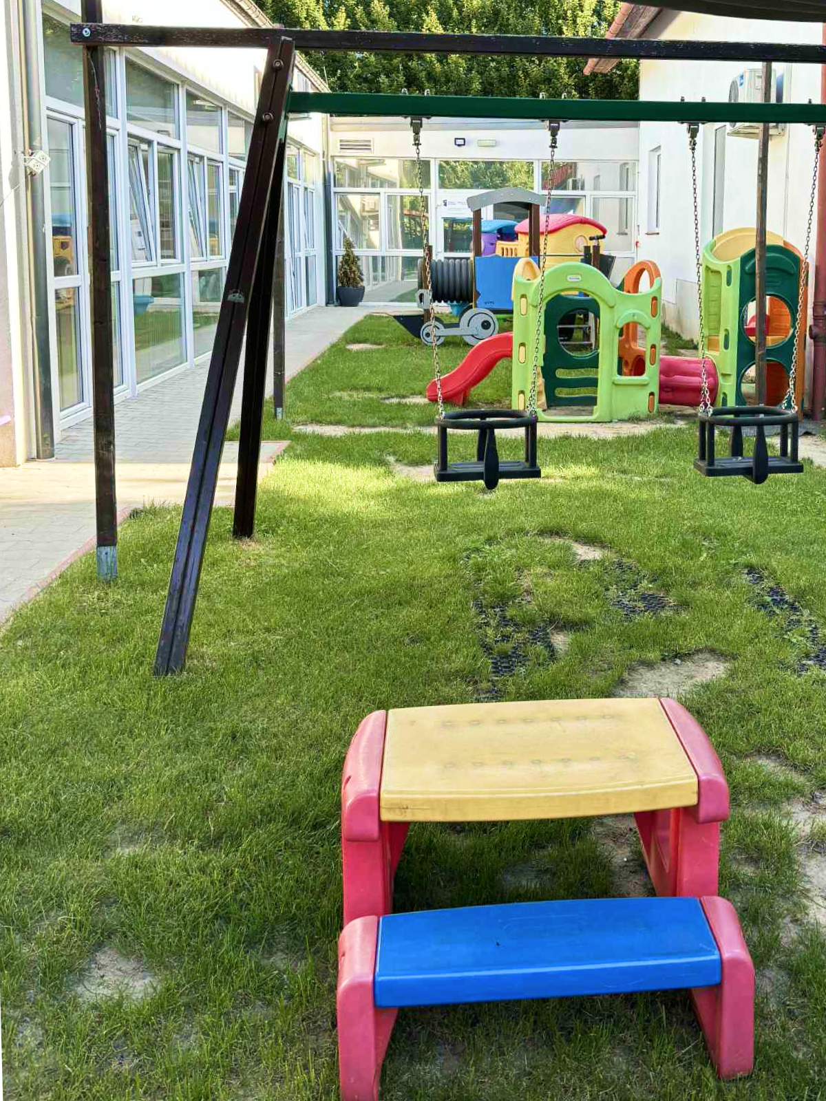 Plac zabaw z huśtawką, kolorowym podestem oraz różnymi kolorowymi elementami placu zabaw w tle.